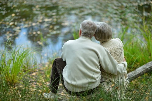 older man and woman sitting together beside lake