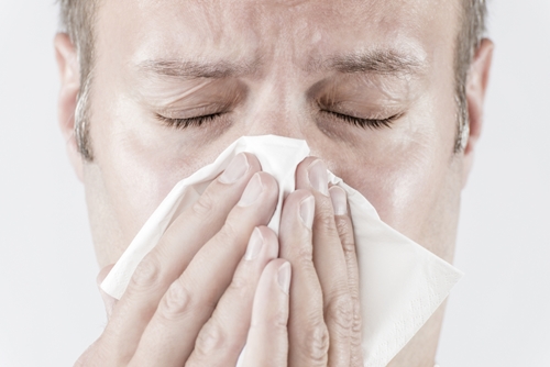 man with seasonal allergies holding tissue to nose