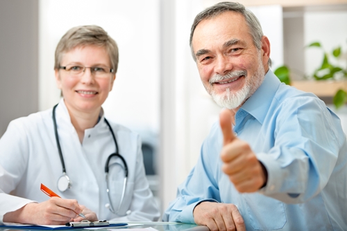older female doctor sites with older male patient while patient gives thumbs up sign
