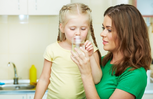young girl drinking water with help of mother
