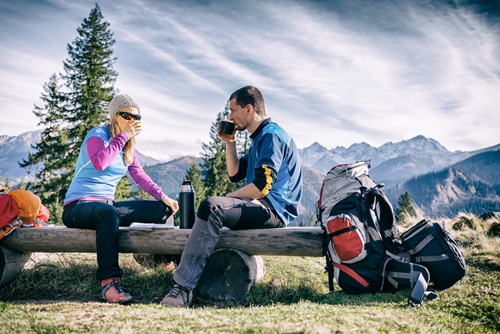 woman and man sit on log while drinking coffee and preparing for their hike