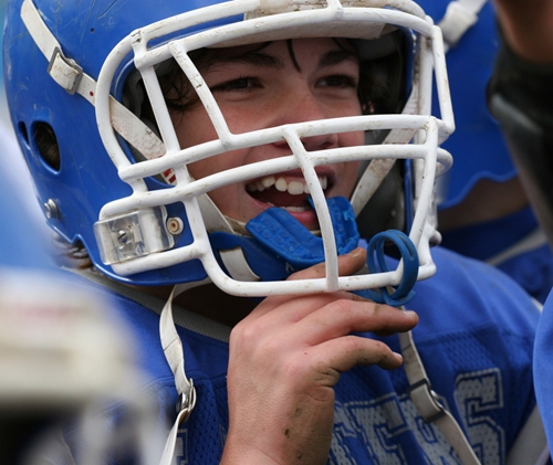 smiling boy wearing football helmet and uniform puts in mouthpiece