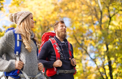man with beard and woman walk in a fall forest with backpacks