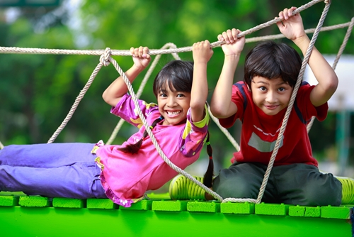 smiling boy and girl play together on a playground rope bridge