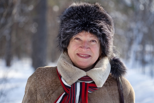 smiling older woman in winter hat and jacket standing in snow