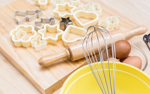 mixing bowl with wisk, cutting board with rolling pin and cookie cutouts on counter