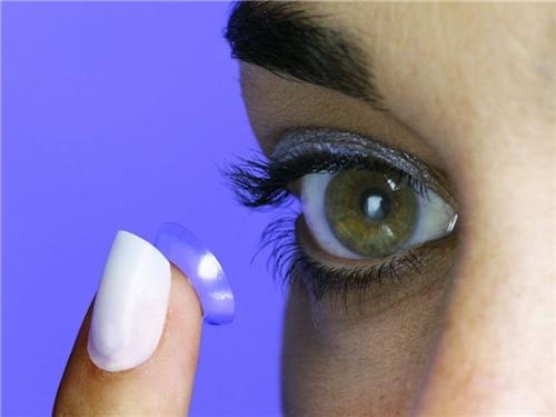 woman holds contact lens in front of eye
