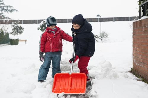 two boys on winter break shovel snow from sidewalk