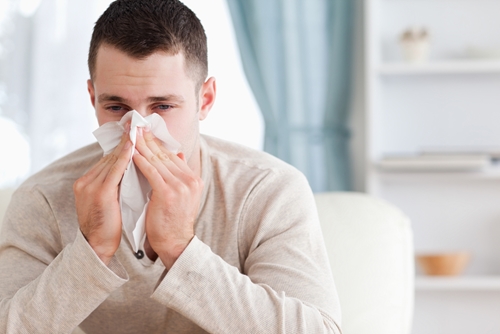 sick man holds tissue to his nose