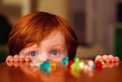 young boy peeks over table to see candy