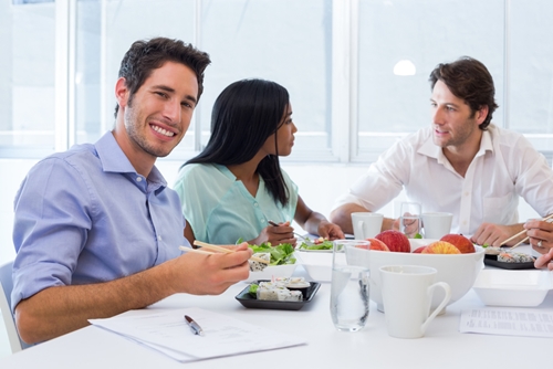 smiling man eats sushi while couple talks at end of table
