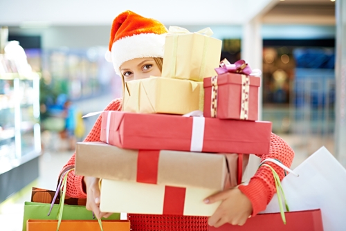 lady wearing a santa hat stands with her arms full of gift wrapped packages