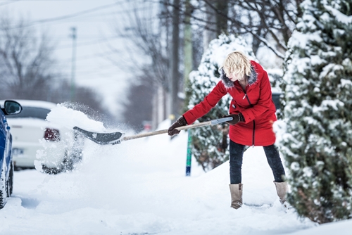 lady in winter coat shovels snow from walkway