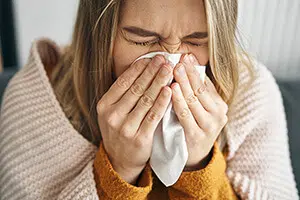 A woman blowing her nose with a tissue