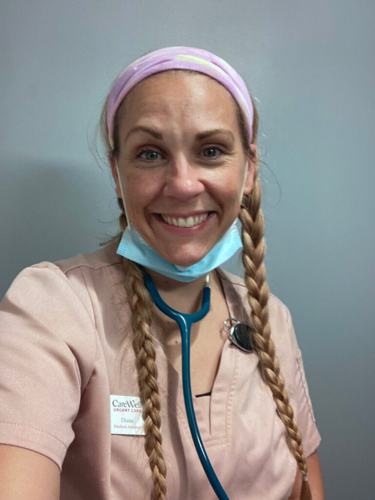 A woman with blond hair and two long braids smiles at the camera. She is wearing a stethoscope, a CareWell badge, and light pink scrubs.