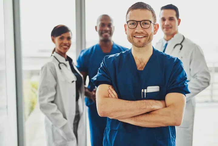 Four physicians smiling at the camera with one Caucasian male physician in the forefront.